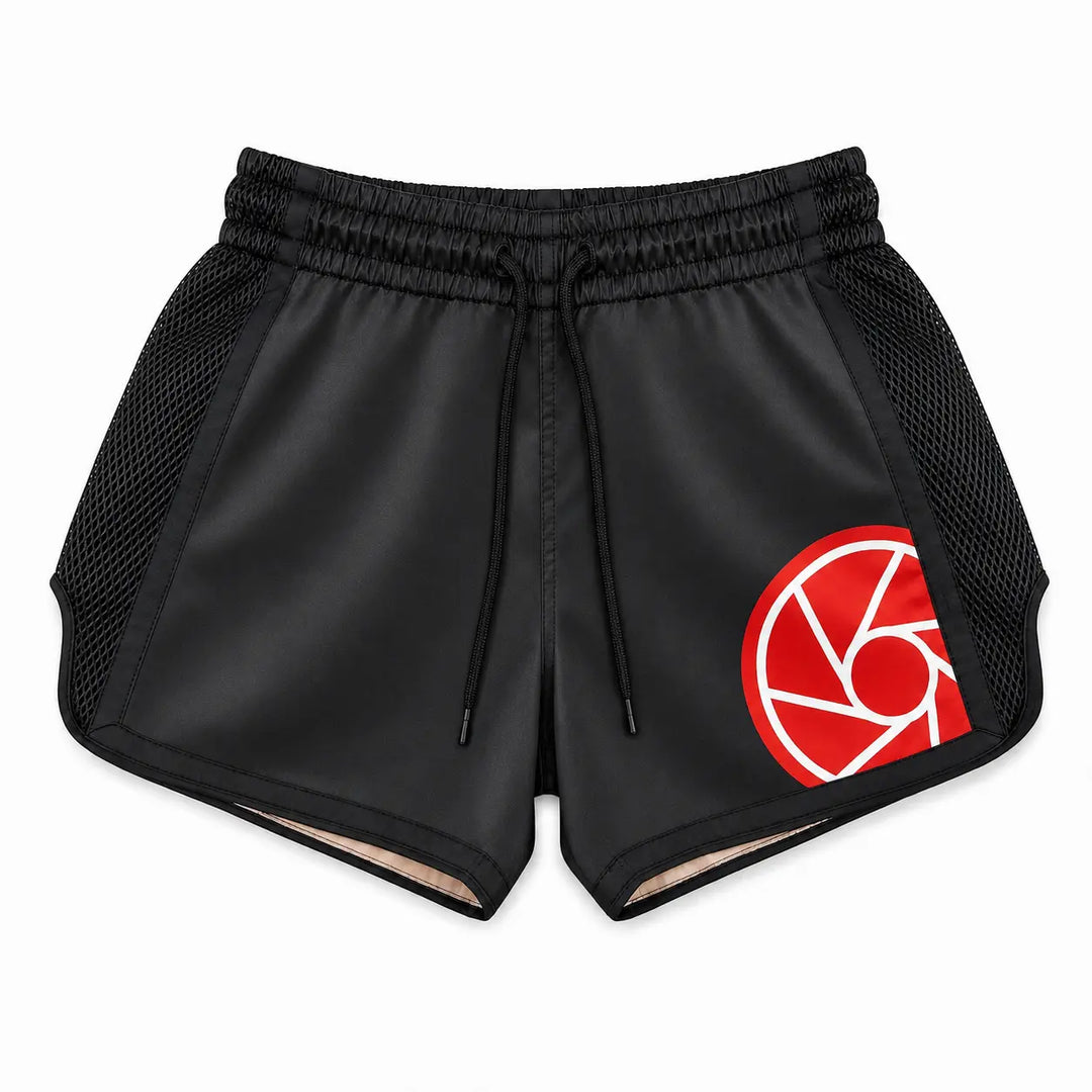 Zwart kickboksbroekje met brede elastische tailleband, verstelbaar koord en zwarte meshpanelen aan de zijkanten. Het rood-witte logo en de ruime pasvorm maken het broekje geschikt voor kickboksen, Muay Thai en intensieve trainingen.