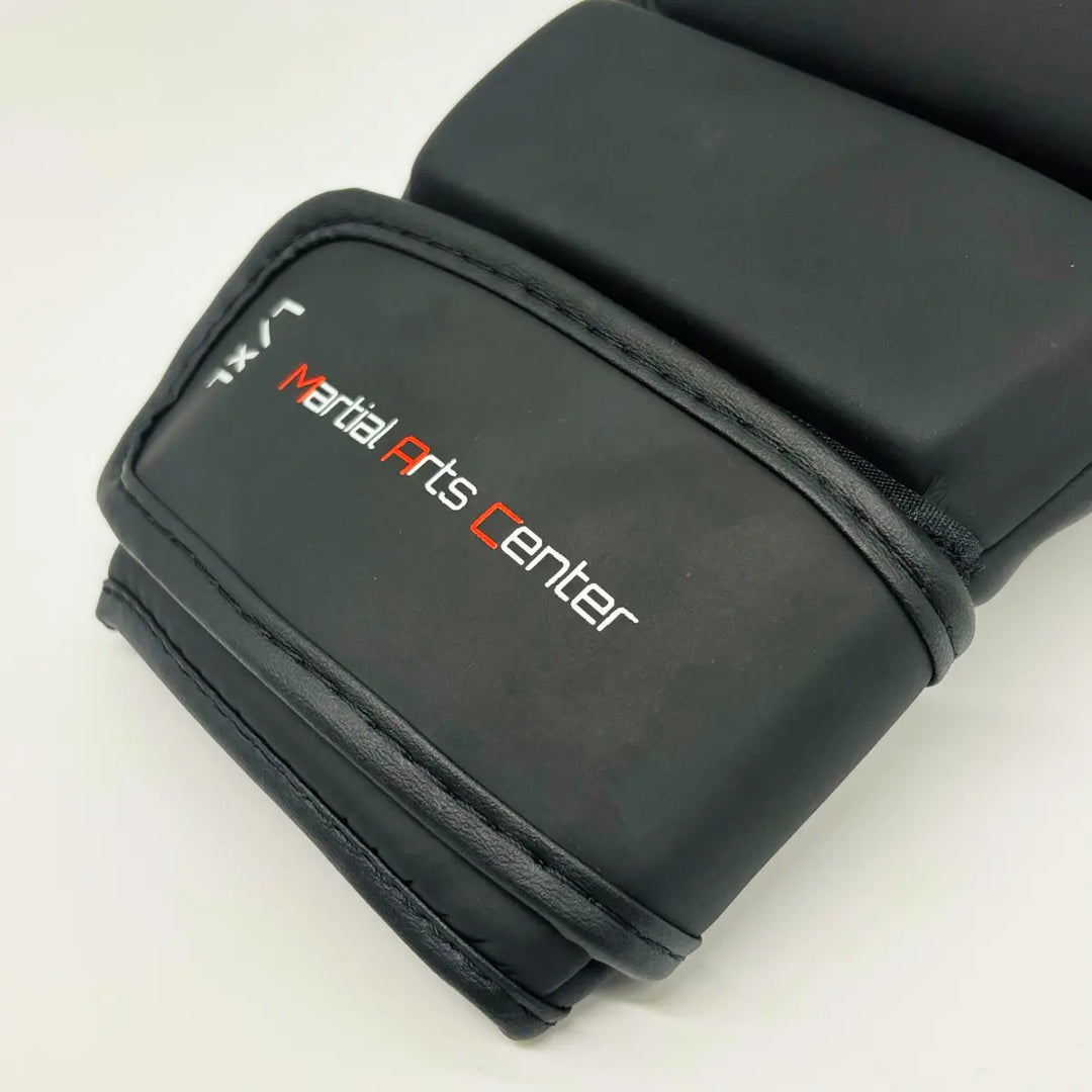 Close-up van zwarte Martial Arts Center MMA-handschoen met brede klittenbandsluiting en wit-rood logo op de pols.
