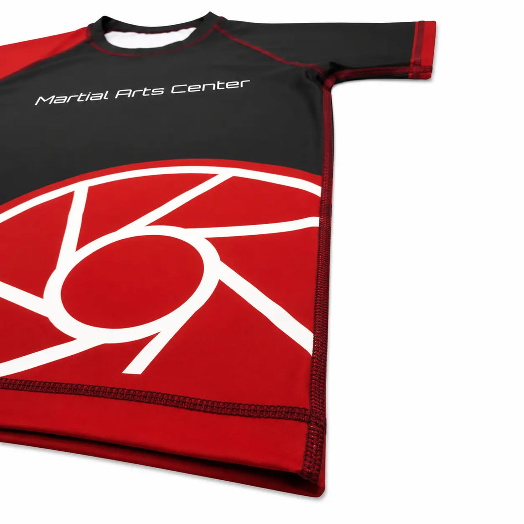 Rood-zwarte rashguard met korte mouwen en Martial Arts Center logo op de borst. De aansluitende pasvorm en gladde sportstof maken het shirt geschikt voor BJJ, grappling, MMA en intensieve trainingen.