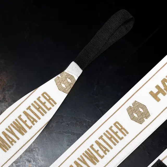 Detail van witte Mayweather Hayabusa handwraps met goudkleurige opdruk en zwarte haaklus voor het veilig vastzetten, geschikt voor bokstraining