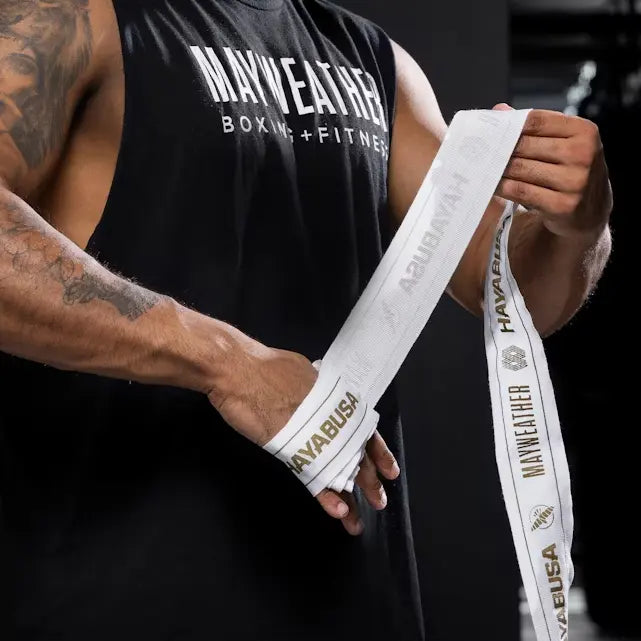 Sportieve man met tattoo wikkelt witte Mayweather Hayabusa handwraps met gouden details om zijn handen in een boksgym, geconcentreerd op voorbereiding voor training