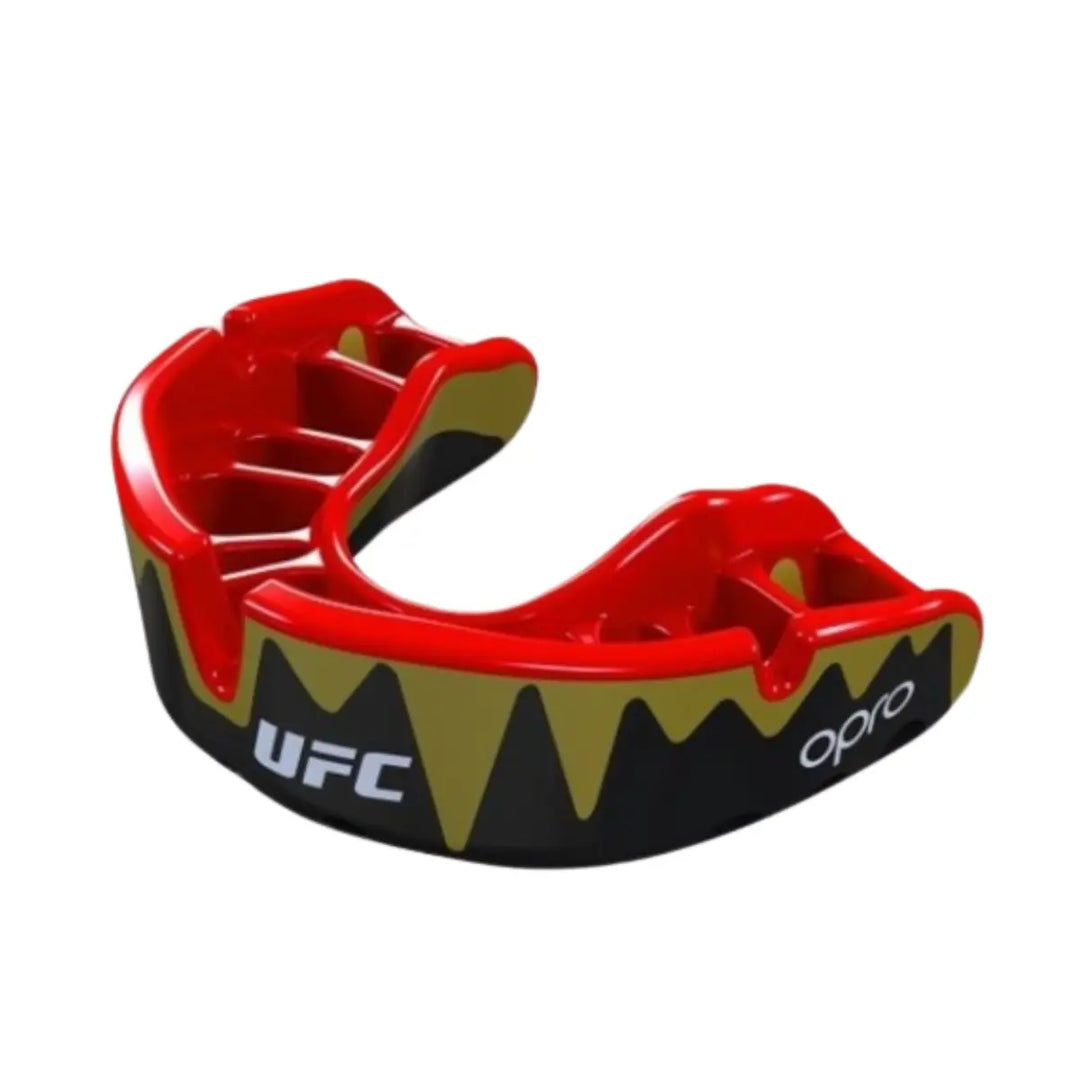 Een zwart, rood en goudkleurig bitje (mondbeschermer) van het merk Opro en met het UFC-logo. De buitenzijde is zwart met een goudkleurig, vlammend patroon en de binnenkant, waar de tanden in gaan, is rood. Het UFC-logo is in wit aan de voorkant zichtbaar.