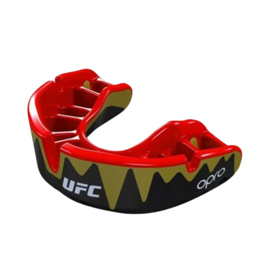 Een zwart, rood en goudkleurig bitje (mondbeschermer) van het merk Opro en met het UFC-logo. De buitenzijde is zwart met een goudkleurig, vlammend patroon en de binnenkant, waar de tanden in gaan, is rood. Het UFC-logo is in wit aan de voorkant zichtbaar.