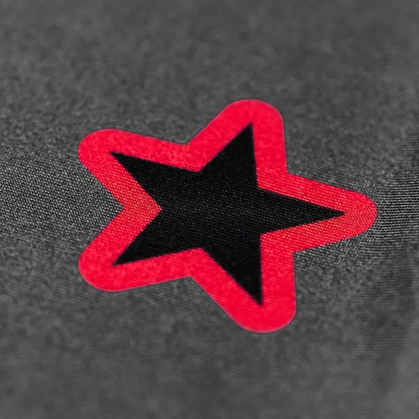 Close-up van de rode en zwarte sterprint op het Yokkao compression shirt in grijs. De afbeelding toont de scherpe randen van de print en het contrast tussen de rode omlijning en de zwarte ster. De fijne structuur van de stof benadrukt de hoogwaardige afwerking en kwaliteit van het materiaal.
