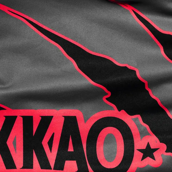 Close-up van het Yokkao-logo en de rode krasdetails op het grijze compression shirt. De afbeelding toont het contrast tussen de zwarte en rode print op de gladde grijze stof. De scherpe lijnen en hoogwaardige afwerking benadrukken het krachtige, dynamische design van het shirt.