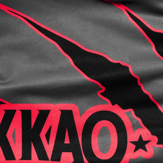 Close-up van het Yokkao-logo en de rode krasdetails op het grijze compression shirt. De afbeelding toont het contrast tussen de zwarte en rode print op de gladde grijze stof. De scherpe lijnen en hoogwaardige afwerking benadrukken het krachtige, dynamische design van het shirt.