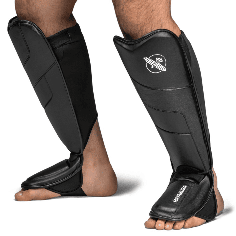 Atleet staat met zwarte Hayabusa T3 Full Back Scheenbeschermers aan, zijaanzicht.