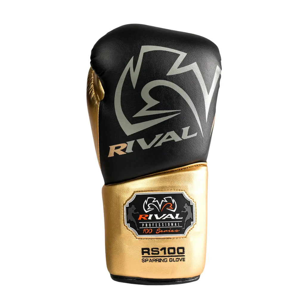 De Rival Bokshandschoen RS100 Professional Zwart Goud is afgebeeld op een witte achtergrond met een elegante combinatie van matzwart en metallic goud. Het grote Rival-logo siert de bovenkant van de handschoen, terwijl het RS100-embleem op de manchet de professionele kwaliteit benadrukt. De foto straalt luxe, kracht en precisie uit, perfect voor boksers die topprestaties eisen.