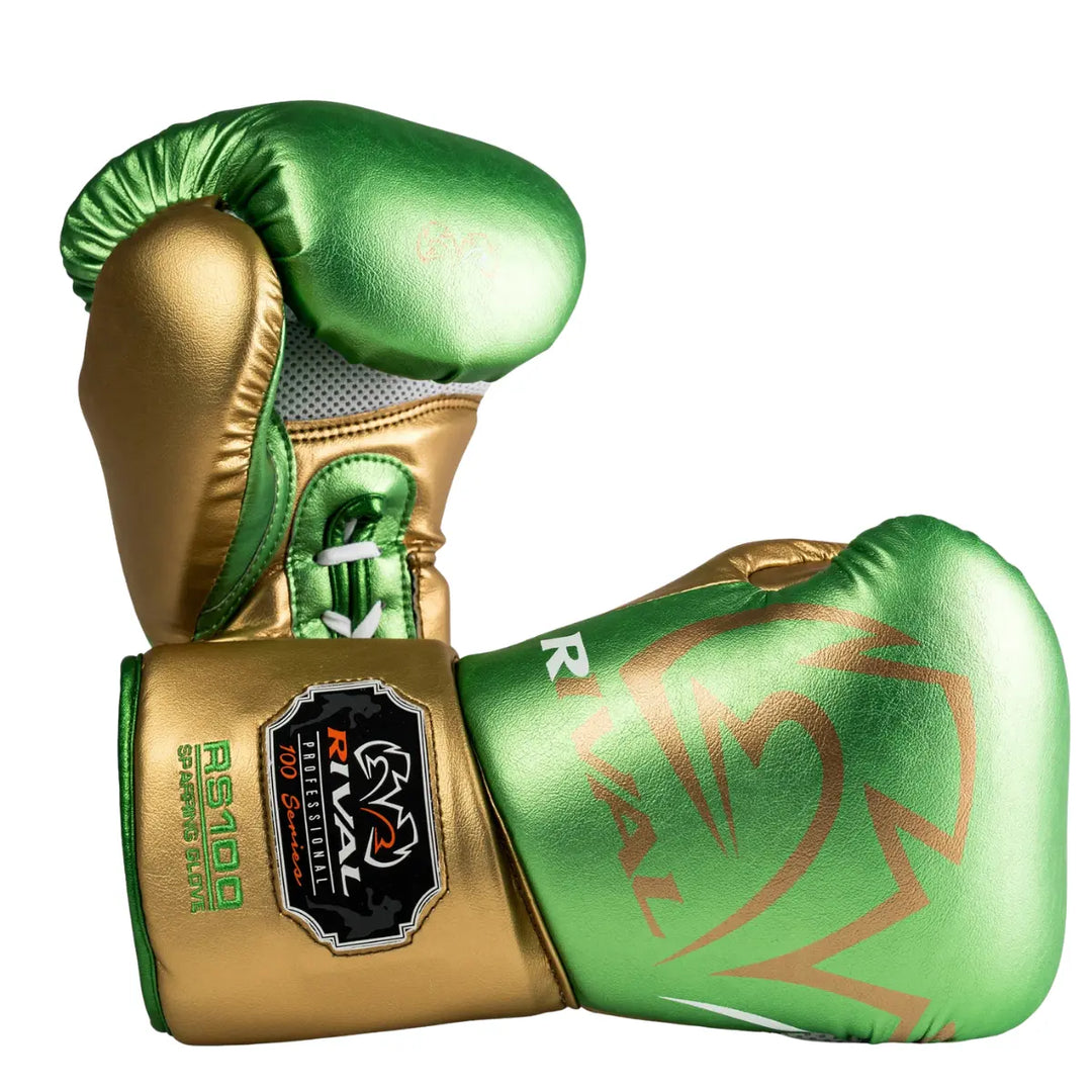 De Rival Bokshandschoenen RS100 Professional Groen Goud liggen gekruist op een witte achtergrond en tonen hun opvallende metallic groene en gouden afwerking. Het grote Rival-logo en het RS100 Professional-embleem zijn duidelijk zichtbaar, terwijl de veterzijde de fijne stiksels en ventilatiezones laat zien. Deze foto benadrukt de luxe uitstraling, technische precisie en professionele kwaliteit van deze exclusieve bokshandschoenen.