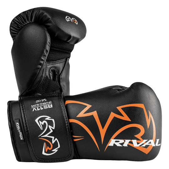 Close-up van de Rival Bokshandschoenen RS11V Evolution Zwart met oranje accenten, liggend in een zijaanzicht. De afbeelding benadrukt het opvallende Rival-logo, de stevige polssluiting met het Evolution-label en de duurzame afwerking van het zwarte leer. Ontworpen voor maximale bescherming en ondersteuning tijdens intensieve bokssessies.