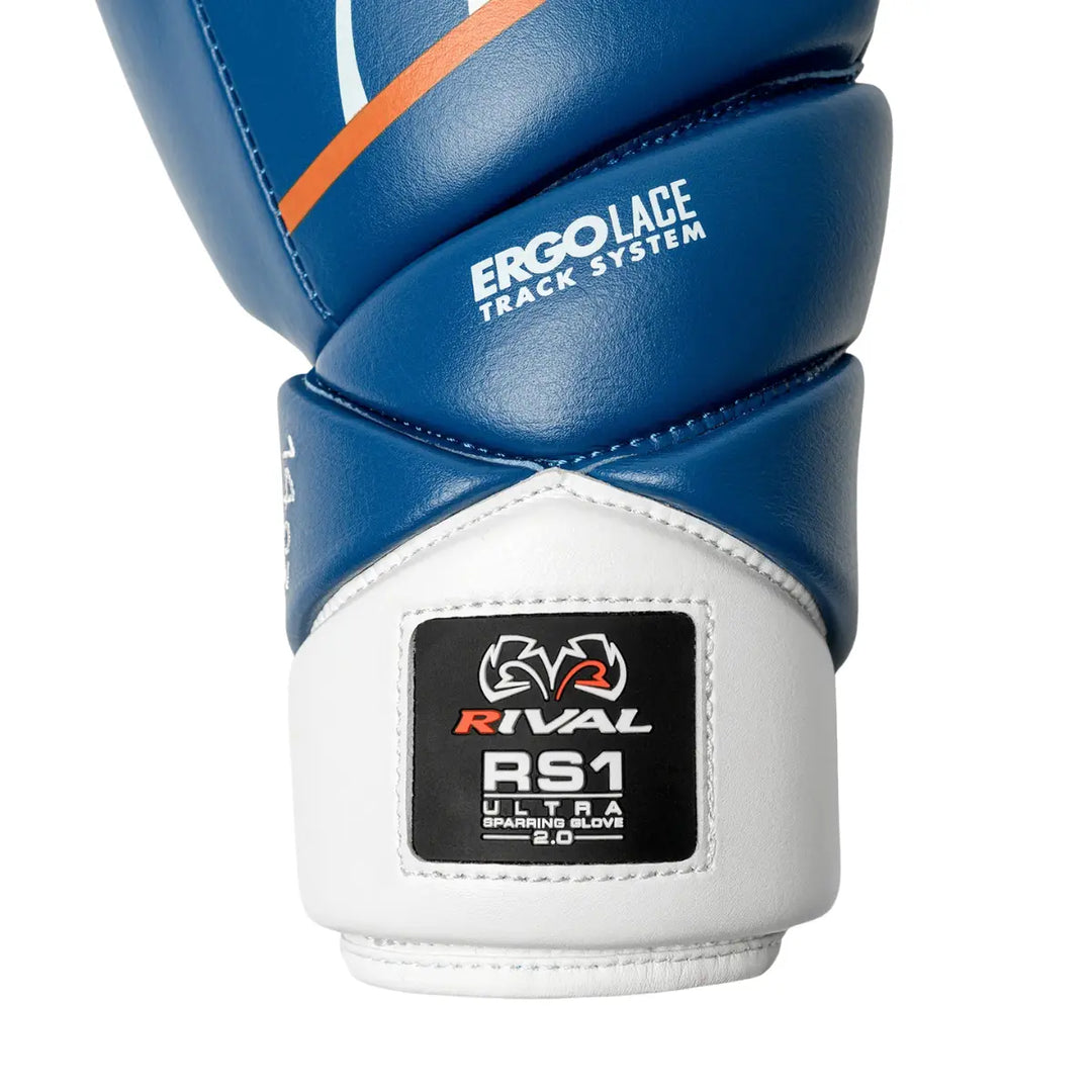 Close-up van de manchet van de Rival RS1 Ultra Sparring Glove 2.0 in blauw en wit. Het label met “RS1 Ultra Sparring Glove 2.0” en het Rival-logo benadrukt de premium afwerking en professionele kwaliteit van dit model.

Boven de manchet is duidelijk het Ergo Lace Track System zichtbaar, dat zorgt voor een gelijkmatige verdeling van de veterspanning en extra polsstabiliteit. De combinatie van stevig kunstleer en nauwkeurige afwerking maakt deze handschoen ideaal voor intensieve bokstraining en sparren, waarb