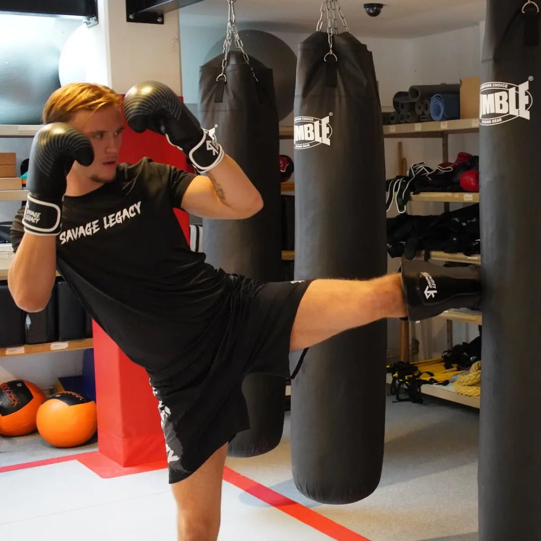 Savage Legacy scheenbeschermers in zwart gedragen door sporter tijdens traptraining op de bokszak in de gym, met scheen- en wreefprotectie zichtbaar in actie.