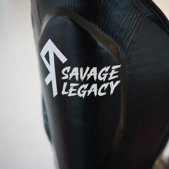 Close-up van Savage Legacy scheenbeschermer in zwart met wit Savage Legacy logo op de scheen, met zichtbaar gevormde padding en stevige afwerking.