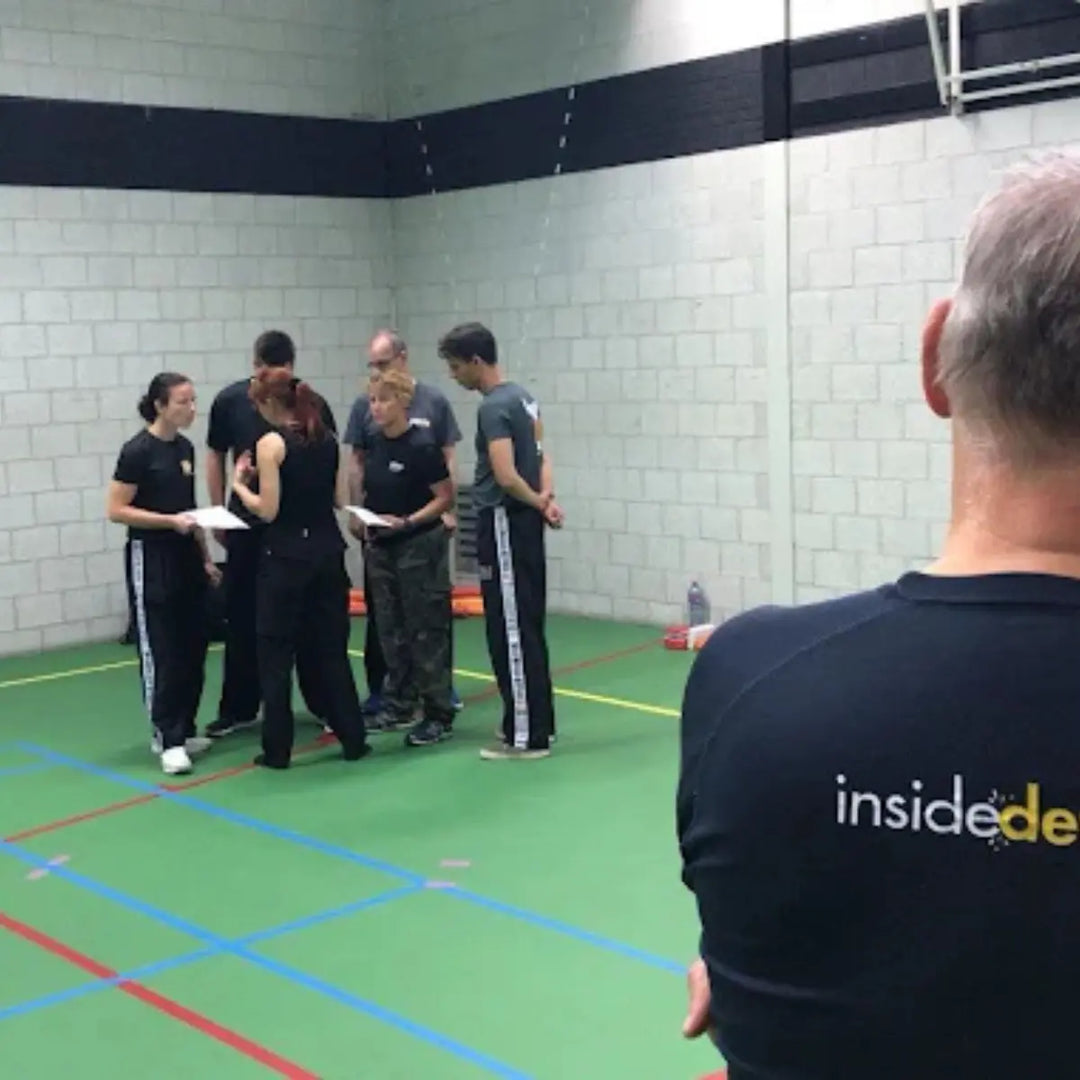 Groepje sporters in sportzaal luistert aandachtig naar uitleg van trainer