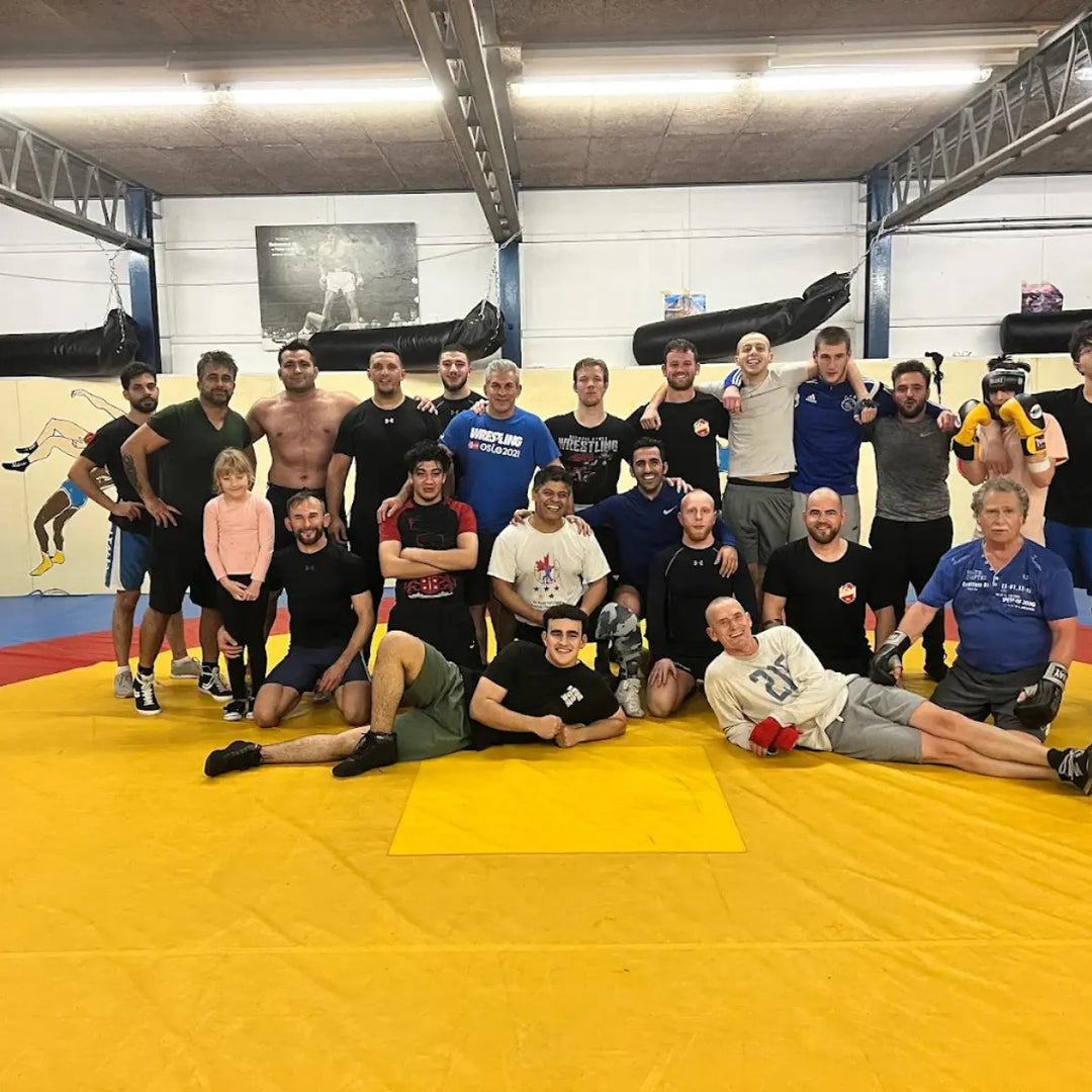 Groep mensen poseert samen op de worstelmat na training