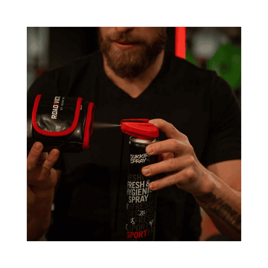 Een man gebruikt Sukkiri Spray op een bokshandschoen om het product te ontsmetten en fris te houden. De spray wordt rechtstreeks op de handschoen aangebracht