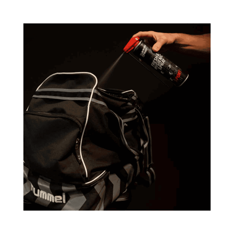 Een persoon spuit Sukkiri Spray in een sporttas om de inhoud te verfrissen en geurtjes te neutraliseren. De zwarte sporttas staat open terwijl de spray wordt aangebracht.