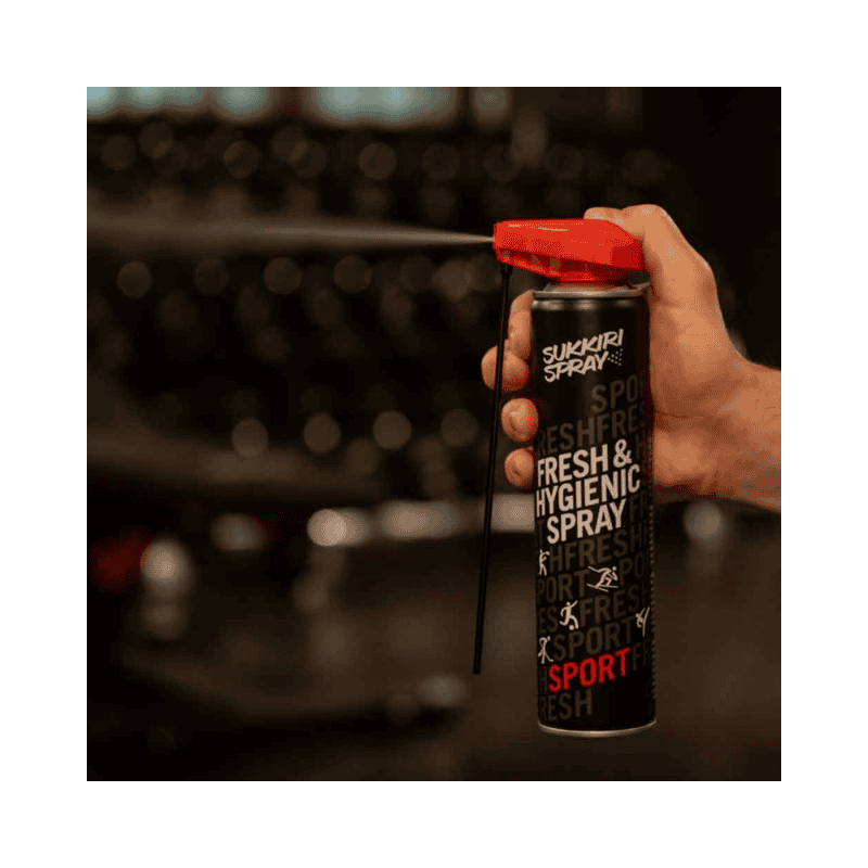Een close-up van een hand die Sukkiri Fresh & Hygienic Spray vasthoudt en de spray activeert zonder een verlengd mondstuk. De spray is klaar voor gebruik in een sportomgeving."