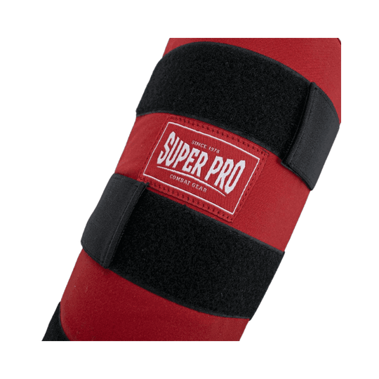 Close-up van het logo "Super Pro" op een rode scheenbeschermer met zwarte klittenbandsluitingen. Het logo bevindt zich in het midden van de beschermer.