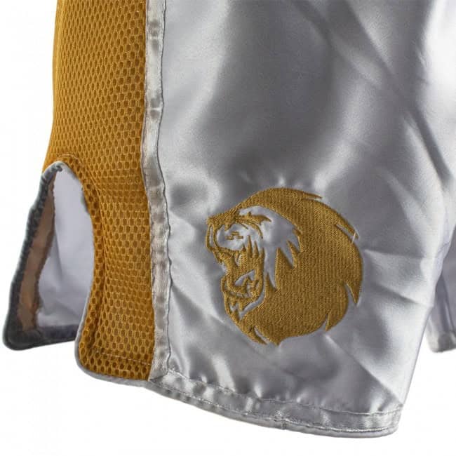 Detailweergave van het Super Pro kickboksbroekje Brave in goud en zilver, met een geborduurd leeuw-logo op het satijnen vlak. Het ontwerp combineert ademend mesh aan de zijkant met een glanzende afwerking aan de voorkant voor optimale ventilatie en stijl tijdens training of wedstrijd.