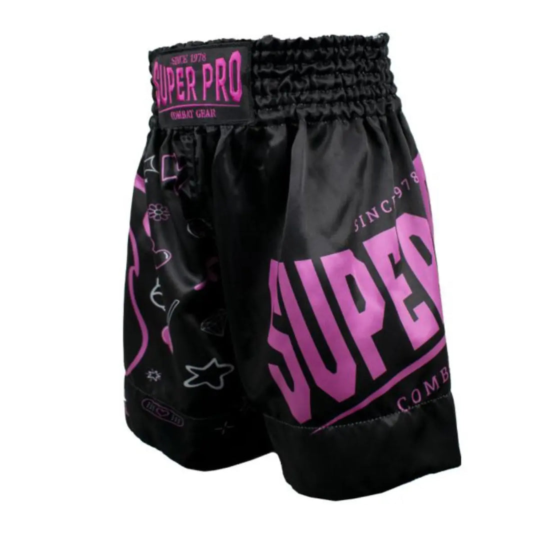 Deze afbeelding toont het Super Pro Kids Bear kickboksbroekje vanuit een schuine hoek, waarbij het grote roze Super Pro-logo prominent zichtbaar is. De zwarte stof is versierd met speelse roze en witte illustraties zoals sterren, hartjes en handschoenen. De brede elastische tailleband met Super Pro-patch zorgt voor een stevige, comfortabele pasvorm.