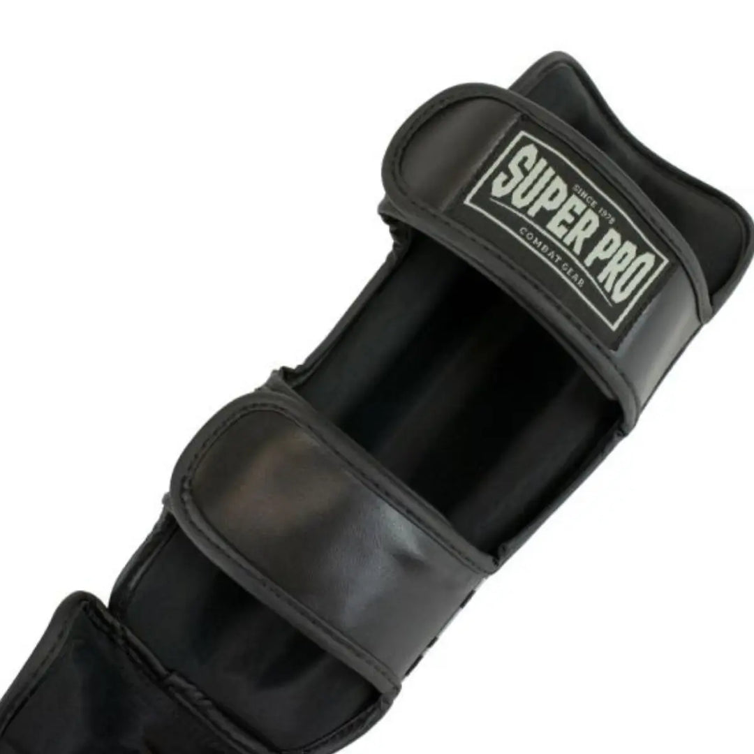 Zwarte scheenbeschermer met twee brede klittenbandsluitingen en een label met de tekst 'Super Pro Combat Gear' aan de bovenkant.