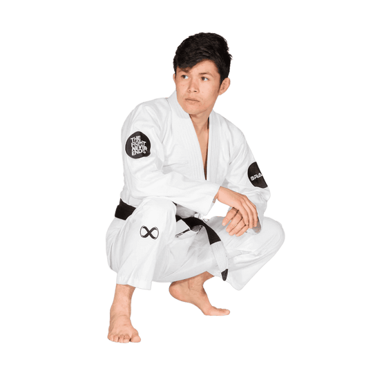 Een afbeelding van een man in een witte BJJ Gi gehurkt in een ontspannen houding, met een focus op het "The Fight Never Ends"-logo op de mouwen en broekspijp. De zwarte band is eveneens zichtbaar.