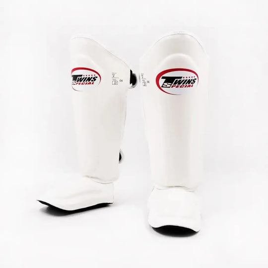Twins Special SGL7 scheenbeschermers in wit met zwart afgewerkte randen en wit-rood logo op het scheenbeen. Voorzien van dikke padding en geïntegreerde voetbescherming voor optimale schokabsorptie tijdens kickboksen en sparren in de gym.