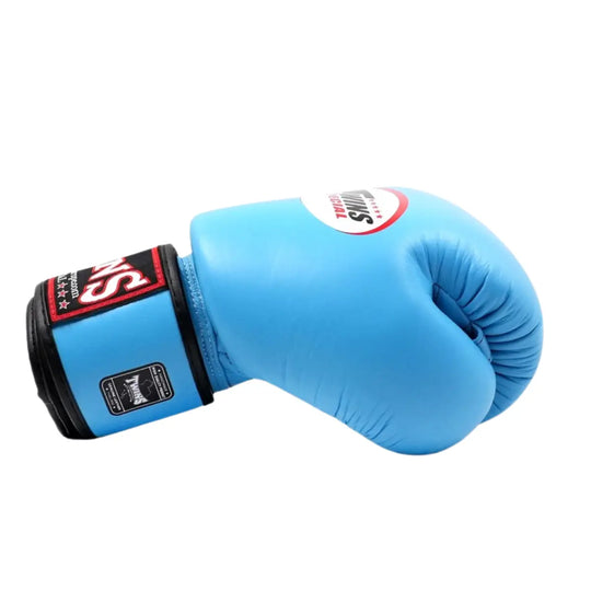 De Twins Bokshandschoen Lichtblauw ligt zijwaarts op een witte achtergrond en toont het iconische Twins-logo op de sluiting. De handschoen is gemaakt van hoogwaardig leer met zwarte accenten en een stevige polssluiting voor extra ondersteuning.
