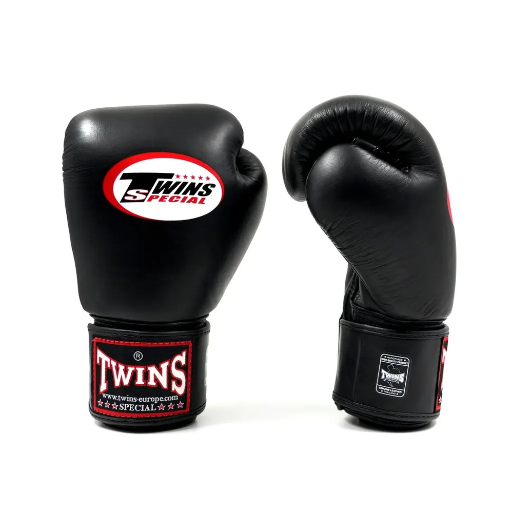 Set zwarte Twins bokshandschoenen op witte achtergrond, rechtopstaand met wit Twins-logo op de vuistzijde en rood label op de polsband.
