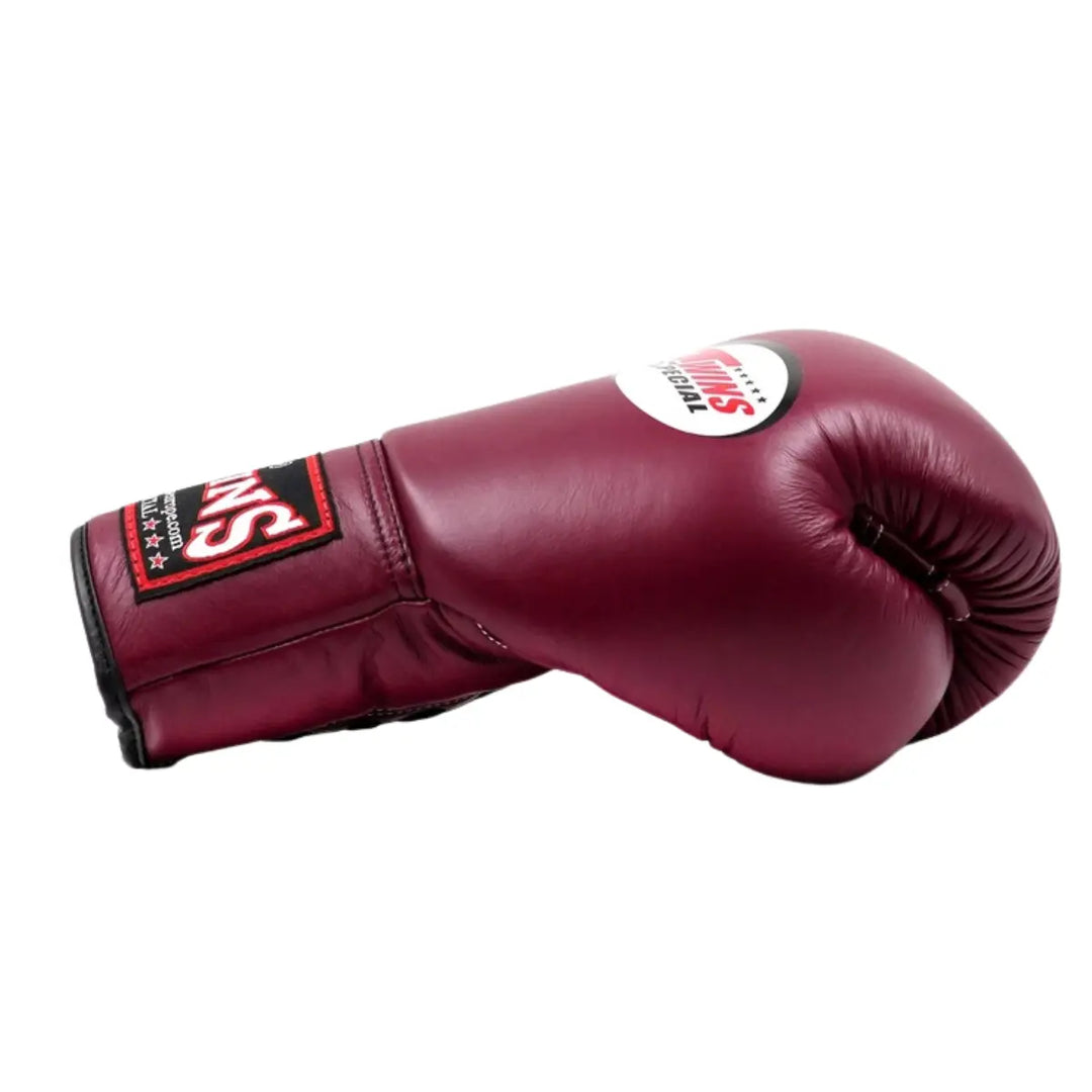 De Twins Bokshandschoen Maroon BGLL 1 ligt zijwaarts op een witte achtergrond en toont de diepe bordeauxrode kleur van het leer. Het Twins Special-logo is zichtbaar bovenop de handschoen, terwijl de zwarte en rode polssluiting zorgt voor contrast en stevigheid. De gladde afwerking en duurzame constructie benadrukken het vakmanschap en de professionele kwaliteit van deze bokshandschoen.