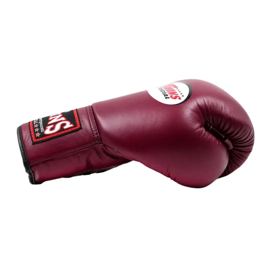 De Twins Bokshandschoen Maroon BGLL 1 ligt zijwaarts op een witte achtergrond en toont de diepe bordeauxrode kleur van het leer. Het Twins Special-logo is zichtbaar bovenop de handschoen, terwijl de zwarte en rode polssluiting zorgt voor contrast en stevigheid. De gladde afwerking en duurzame constructie benadrukken het vakmanschap en de professionele kwaliteit van deze bokshandschoen.
