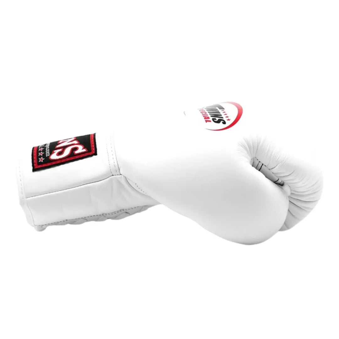 De Twins Bokshandschoen Wit BGLL 1 ligt zijwaarts op een witte achtergrond en toont de strakke, minimalistische uitstraling van het gladde witte leer. Het Twins Special-logo staat duidelijk zichtbaar op de bovenkant, terwijl de zwarte en rode details op de polssluiting voor contrast zorgen. De foto benadrukt het vakmanschap, de kwaliteit en de professionele afwerking van deze luxe bokshandschoen.