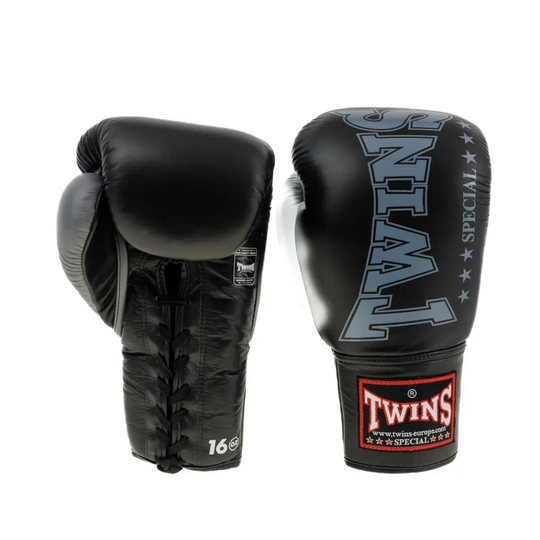 Een paar Twins bokshandschoenen in zwart met grijze details. De foto toont zowel de voorzijde met het Twins-logo als de achterzijde met veter­sluiting en 16 oz markering. Gemaakt voor intensieve bokssessies met maximale steun en duurzaamheid.