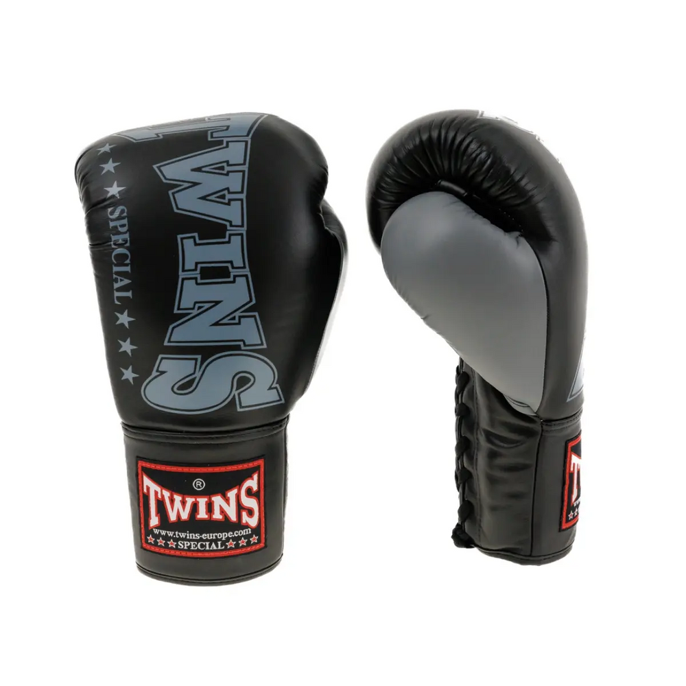 Een paar Twins bokshandschoenen in zwart en grijs, met het herkenbare Twins-logo op de polsband. De handschoenen hebben een glanzende afwerking, vetersluiting en stevige padding, ontworpen voor maximale bescherming en comfort tijdens bokstraining.