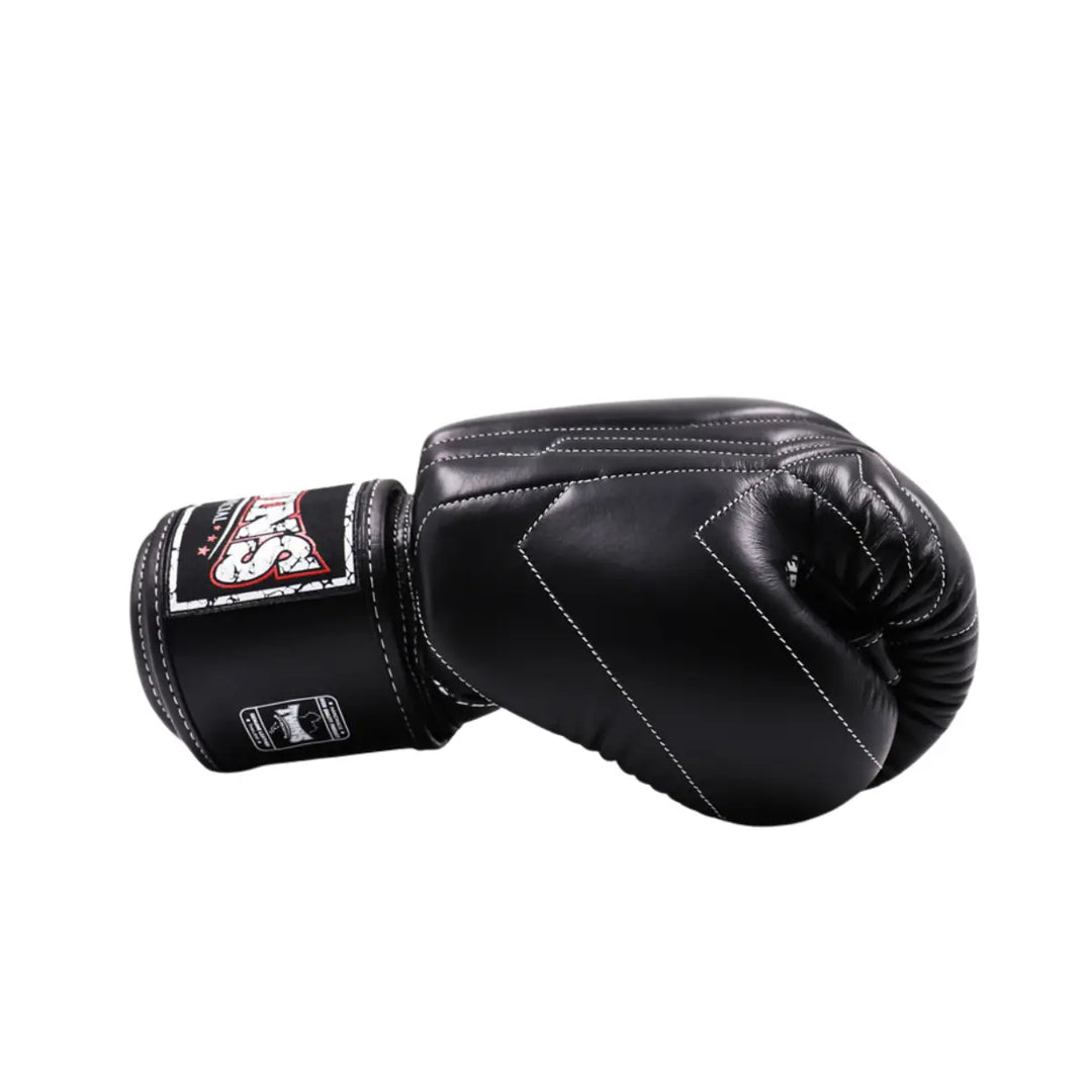 Zijaanzicht van een zwarte Twins Special bokshandschoen met witte stiksels en stevig klittenband. De vorm toont de ergonomische pasvorm en afwerking.