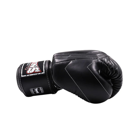 Zijaanzicht van een zwarte Twins Special bokshandschoen met witte stiksels en stevig klittenband. De vorm toont de ergonomische pasvorm en afwerking.