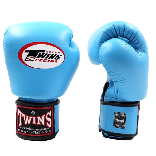 De Twins Bokshandschoenen BGVL3 Lichtblauw zijn afgebeeld op een witte achtergrond, met één handschoen rechtop en de andere schuin gedraaid om de vorm te tonen. Het herkenbare Twins Special-logo is duidelijk zichtbaar op de polssluiting en bovenop de handschoen. De lichtblauwe kleur, leren afwerking en stevige klittenbandsluiting benadrukken de premium kwaliteit en duurzaamheid die geschikt is voor intensieve bokssessies.