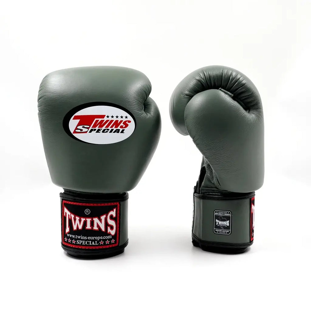 Set olijfgroene Twins bokshandschoenen, rechtopstaand op een witte achtergrond met wit Twins-logo op de vuistzijde en rood label op de polsband.