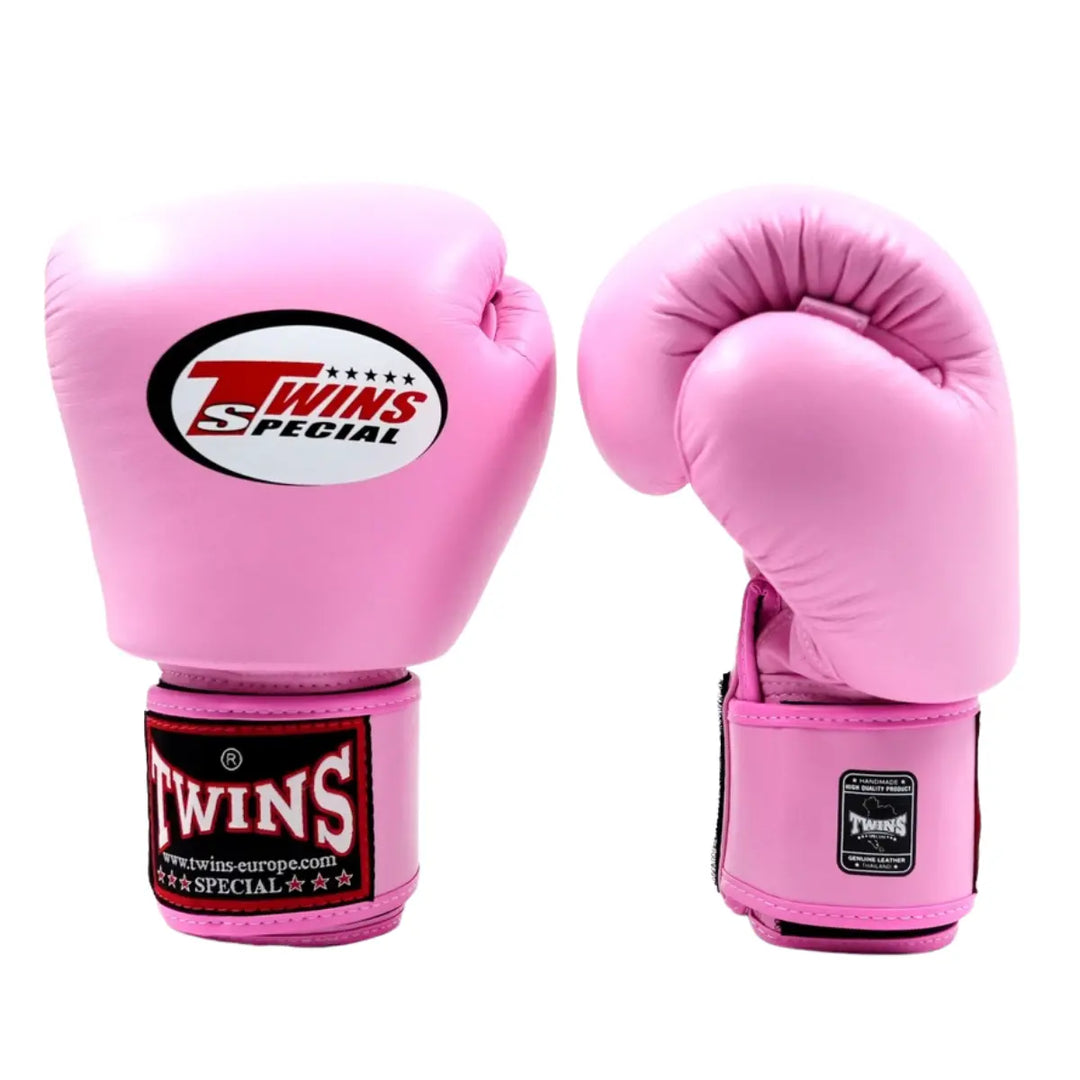 De Twins Bokshandschoenen BGVL3 Roze staan rechtop naast elkaar op een witte achtergrond. De ene handschoen toont de voorzijde met het Twins Special-logo, terwijl de andere in een licht gebogen positie de pasvorm en stiksels laat zien. De roze leren afwerking, zwarte details en stevige polssluiting benadrukken de kwaliteit en het stijlvolle ontwerp voor serieuze bokstrainingen.