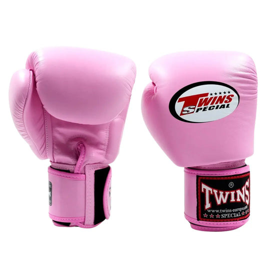 De Twins Bokshandschoenen Roze BGVL3 staan rechtop naast elkaar op een witte achtergrond. De handschoenen hebben een opvallende roze kleur met het kenmerkende Twins Special-logo op de bovenkant en op de stevige polssluiting. De gladde leren afwerking en het ergonomische ontwerp benadrukken de combinatie van stijl, comfort en bescherming voor intensieve bokstrainingen.