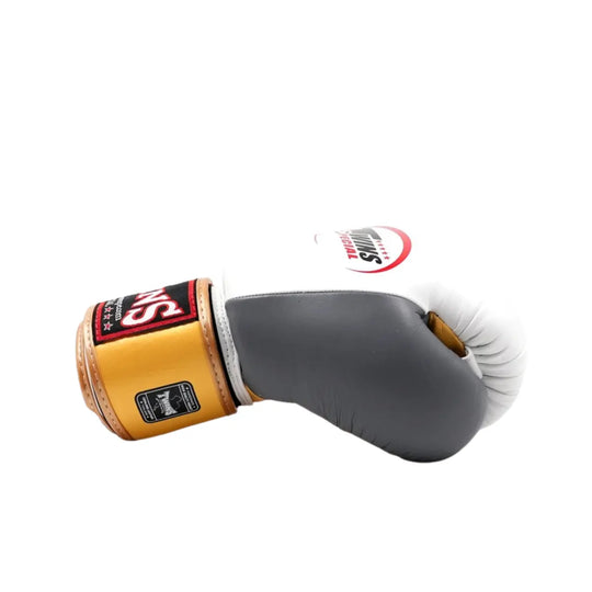 Zijkant van de Twins Bokshandschoenen BGVL 4 Goud met wit-grijze stootzone en goudkleurige polsband. De ergonomische vorm en dikke padding zijn duidelijk zichtbaar. Deze bokshandschoen is ontworpen voor intensieve bokstraining en biedt optimale bescherming en comfort.