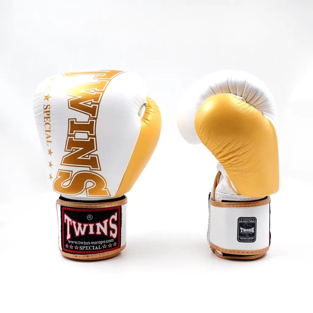 Set Twins bokshandschoenen in wit en goud, rechtopstaand op een witte achtergrond met groot TWINS-logo op de vuistzijde en rood label op de polsband.