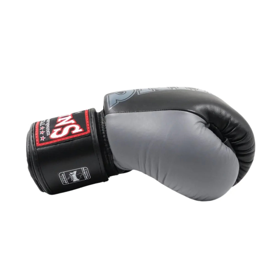 Zwart-grijze bokshandschoen van het merk Twins, liggend op een witte achtergrond met zichtbaar rood logo op de polsband.