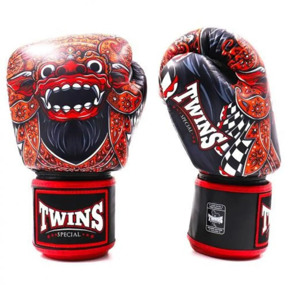 Twee Twins bokshandschoenen met rood fantasy-design en Balinees maskermotief. De ene handschoen toont de gedetailleerde voorkant met het gezicht van de mythische figuur, terwijl de andere de zijkant met het Twins-logo en sierlijke patronen laat zien. Ontworpen voor kracht, stijl en bescherming tijdens bokstrainingen.