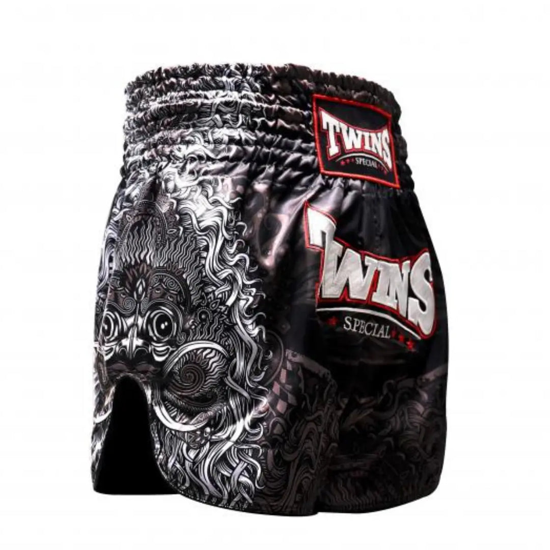 Zijaanzicht van het Twins Special kickboksbroekje in zwart met een opvallende, witte drakenprint op de zijkant. Het glanzende satijn polyester geeft de short een premium uitstraling, terwijl het diepe splitje aan de zijkant zorgt voor optimale bewegingsvrijheid bij trappen. Het grote TWINS-logo met rode accenten springt eruit op de dij. Ideaal voor kickboksers die kracht, traditie en stijl willen combineren in hun outfit.