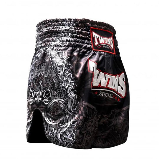 Zijaanzicht van het Twins Special kickboksbroekje in zwart met een opvallende, witte drakenprint op de zijkant. Het glanzende satijn polyester geeft de short een premium uitstraling, terwijl het diepe splitje aan de zijkant zorgt voor optimale bewegingsvrijheid bij trappen. Het grote TWINS-logo met rode accenten springt eruit op de dij. Ideaal voor kickboksers die kracht, traditie en stijl willen combineren in hun outfit.
