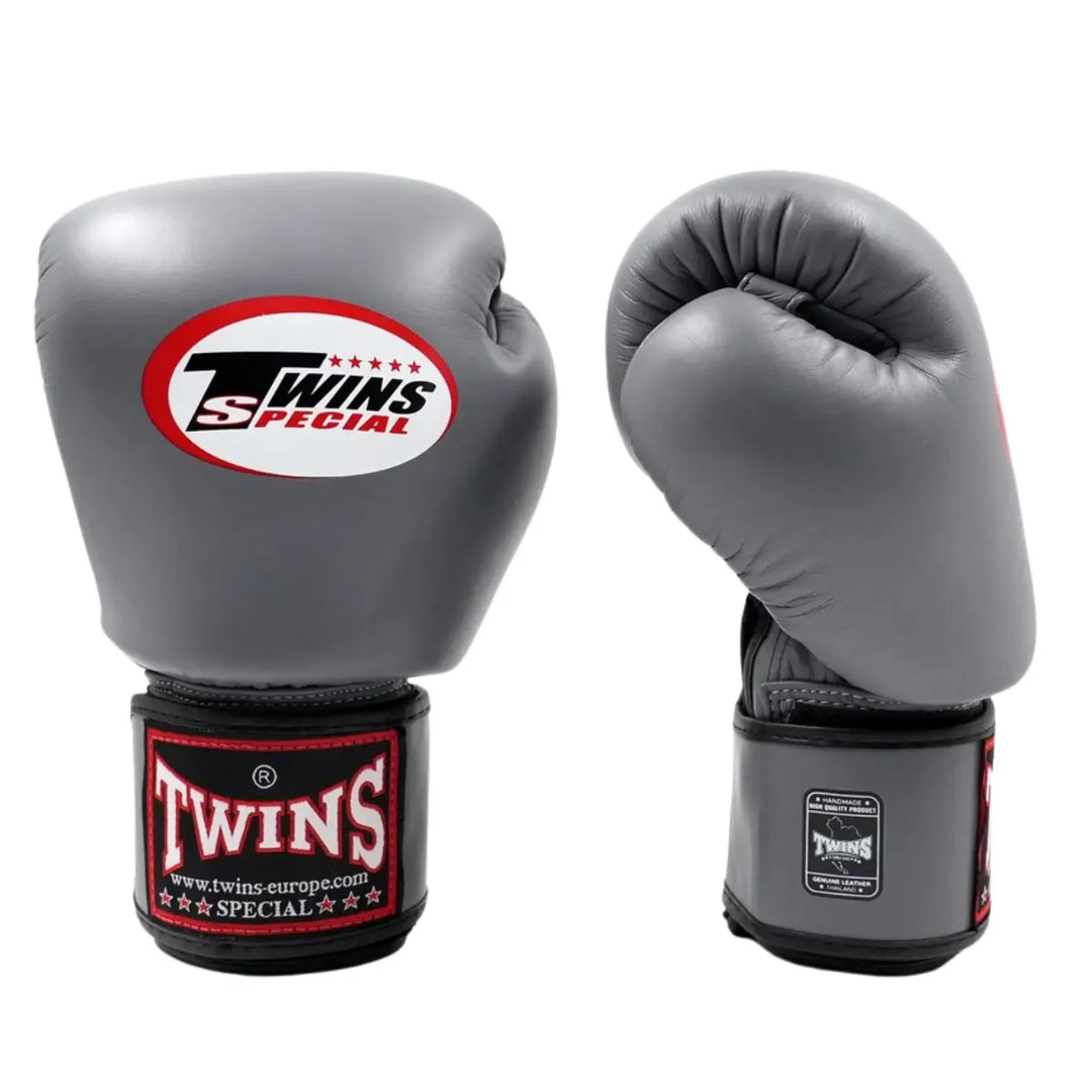 Twins Special Bokshandschoenen Grijs – Paar hoogwaardige leren bokshandschoenen in stijlvolle grijze kleur met zwart-rode polsband en het iconische Twins-logo. Bieden maximale bescherming, uitstekende demping en stevige polsondersteuning tijdens bokstraining en sparring. Perfect voor boksers die comfort, duurzaamheid en prestaties willen combineren.