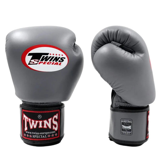 Twins Special Bokshandschoenen Grijs – Paar hoogwaardige leren bokshandschoenen in stijlvolle grijze kleur met zwart-rode polsband en het iconische Twins-logo. Bieden maximale bescherming, uitstekende demping en stevige polsondersteuning tijdens bokstraining en sparring. Perfect voor boksers die comfort, duurzaamheid en prestaties willen combineren.