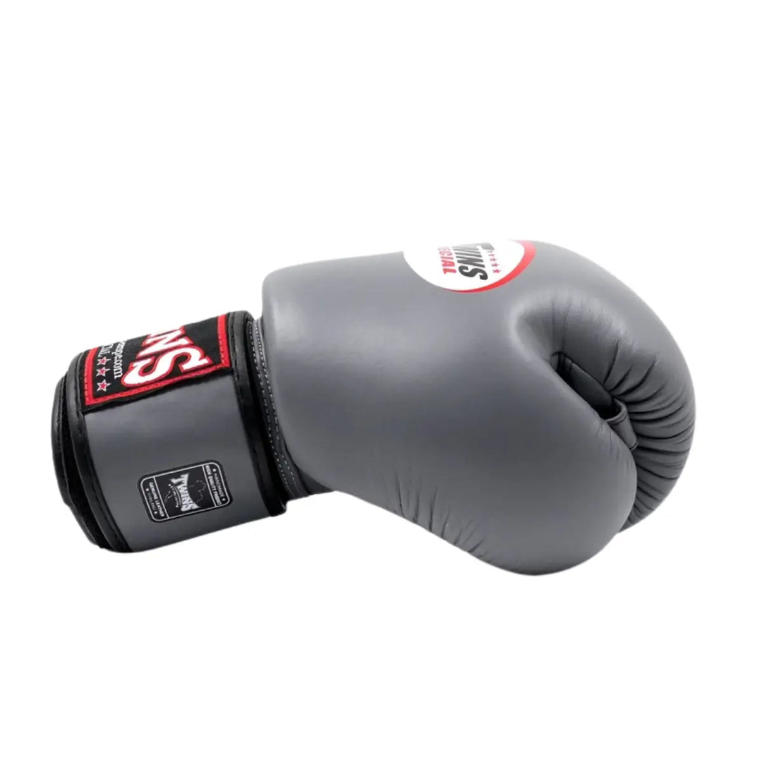 Twins Special Bokshandschoen Grijs – Zijaanzicht van een premium leren bokshandschoen in elegante grijze kleur met zwart-rode polsband en Twins-logo. Ontworpen voor optimale demping, stabiliteit en polsondersteuning tijdens bokstraining en sparring. Perfect voor boksers die kwaliteit en duurzaamheid waarderen.